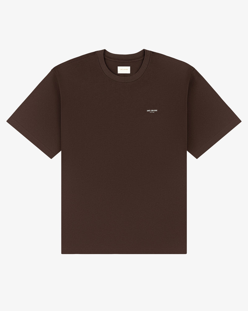 The Micro Logo Tee is a plain brown short-sleeve T-shirt with a small white text logo on the left chest.