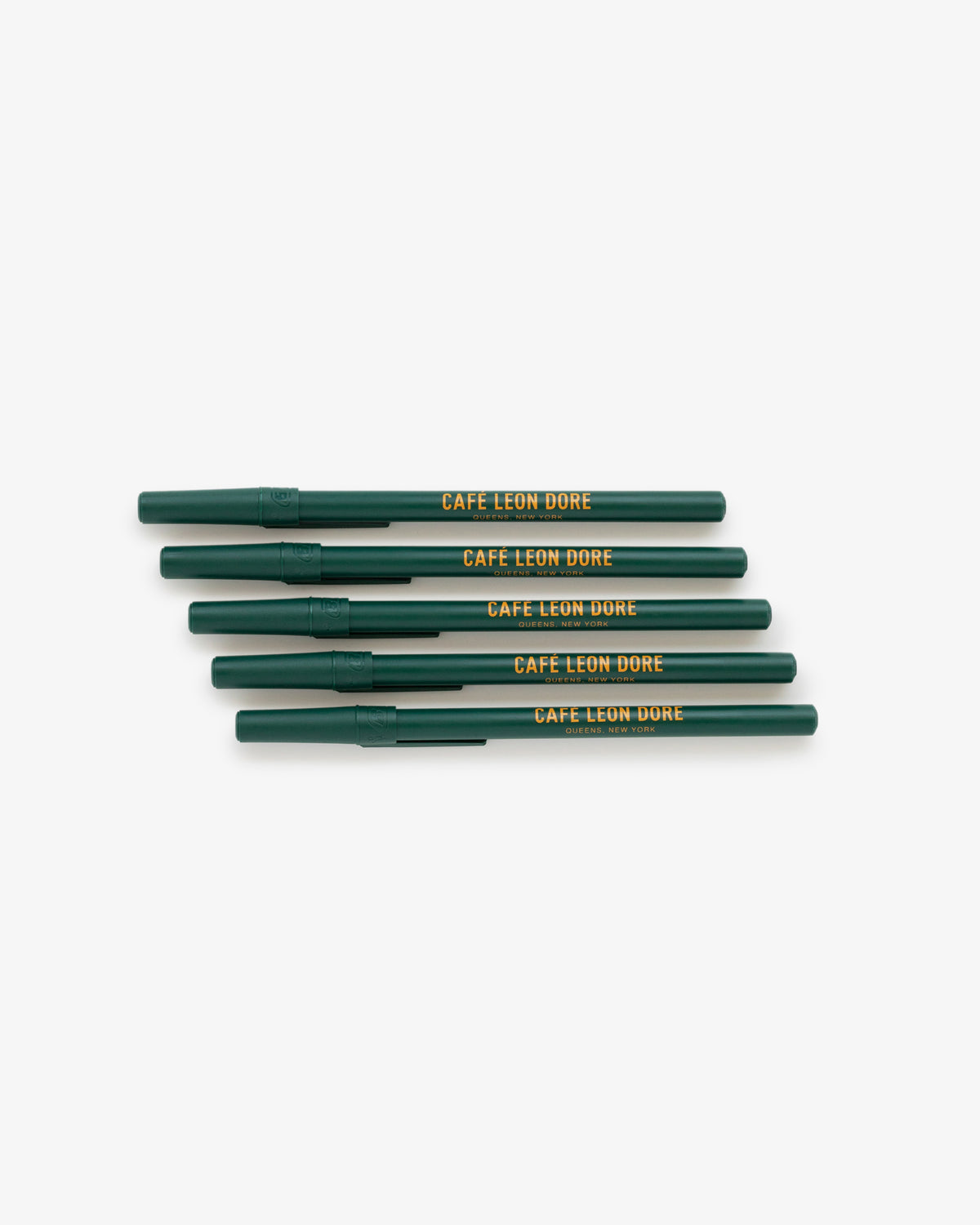 Five green Café Leon Dore Ballpoint Pens with yellow text, stacked diagonally on a white background.