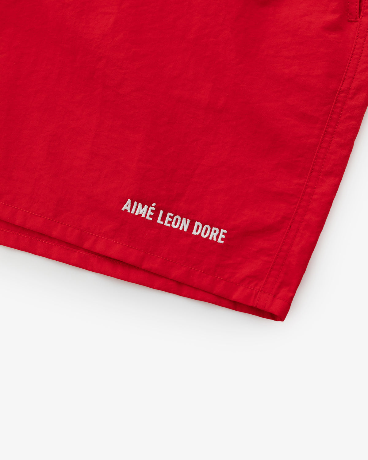 Close-up of Logo Swim Short in red with AIMÉ LEON DORE in white near the hem on a plain background.