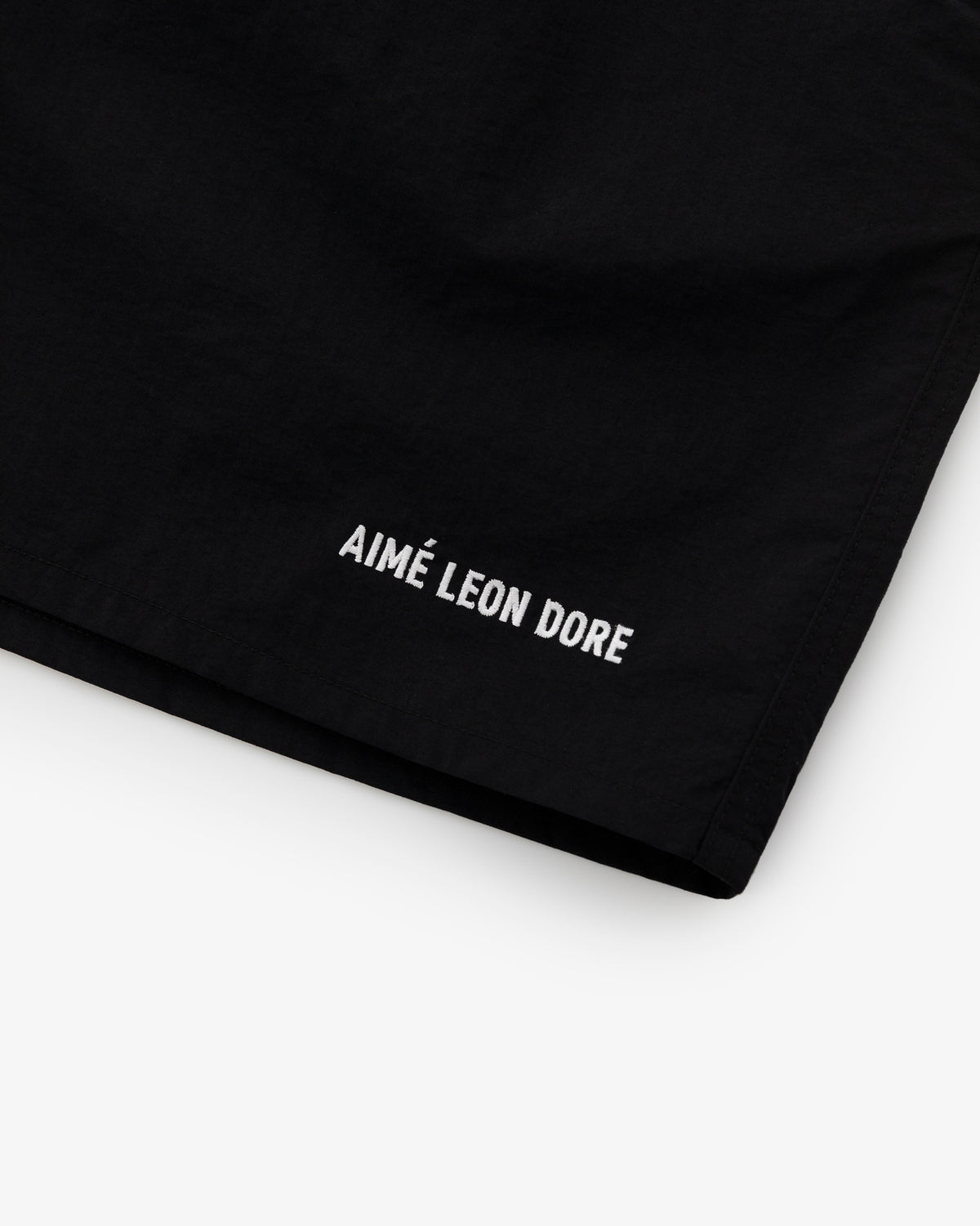 Black Logo Swim Short featuring AIMÉ LEON DORE white embroidery near the hem, shown on a white background.
