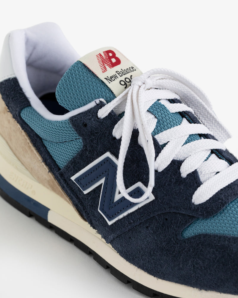 Close-up of a New Balance Made in USA 996 sneaker in blue, navy, and beige with white laces and red tongue branding.