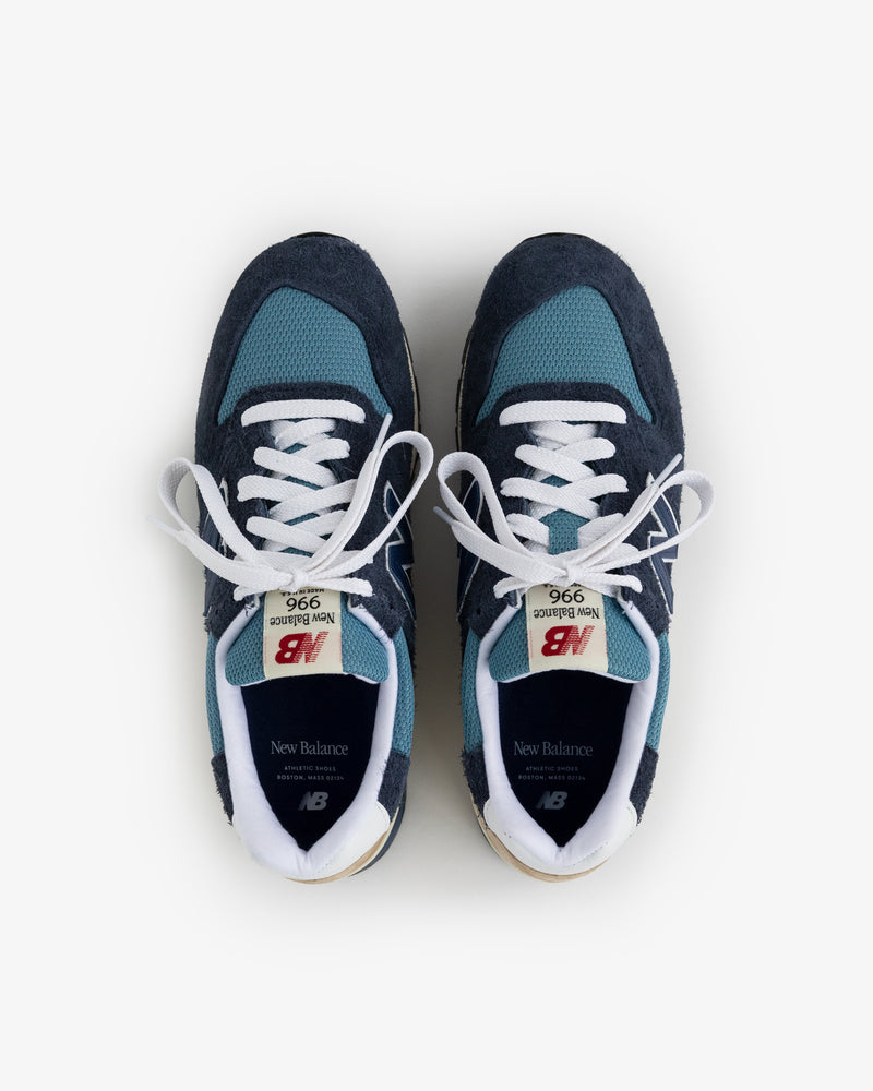 A pair of New Balance Made in USA 996 sneakers in navy and teal with white laces, viewed from above on white.