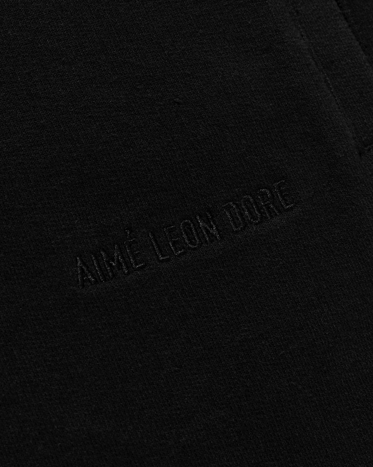 Close-up of black fabric on Tonal Logo Sweatshorts with AIMÉ LEON DORE embroidered in matching black thread.